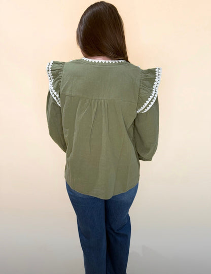 Back view of olive green blouse with ruffled shoulders and cream trim, styled casually with denim jeans.
