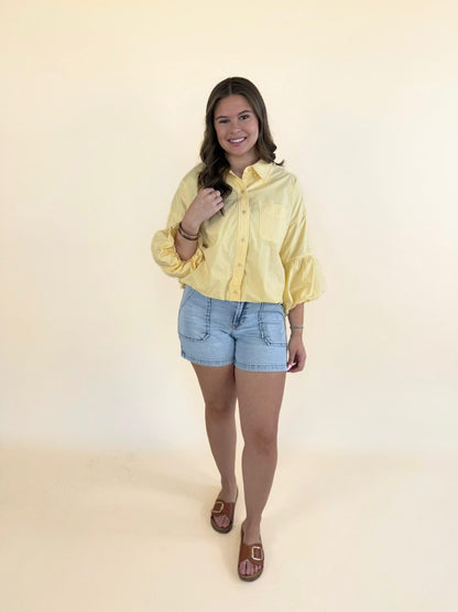 Woman styling yellow bubble sleeve top with denim shorts and brown slide sandals for spring outfit