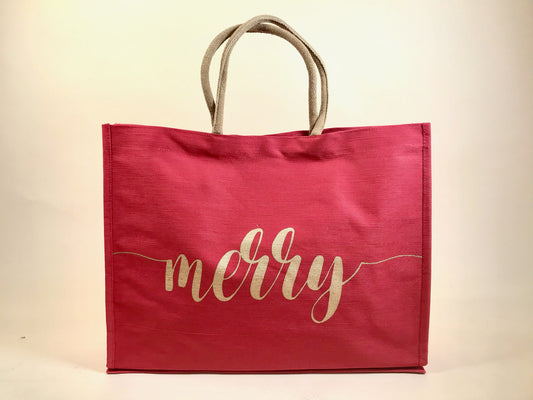 Large red holiday tote bag with gold “merry” script and rope handles against neutral backdrop