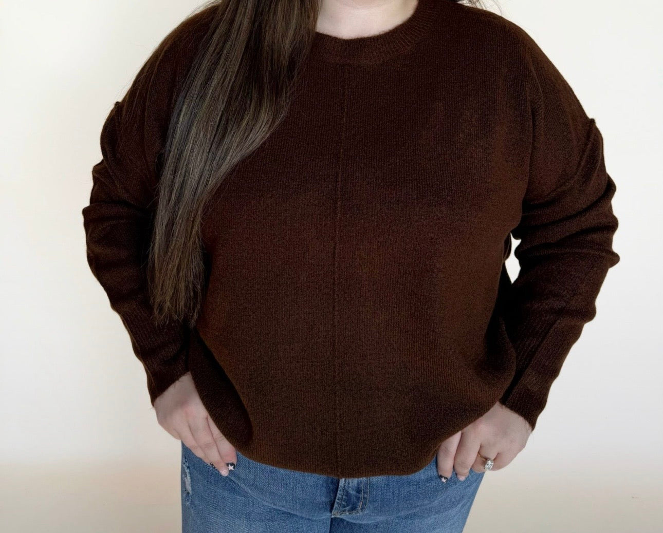 Person wearing a brown sweater and blue jeans against a plain background