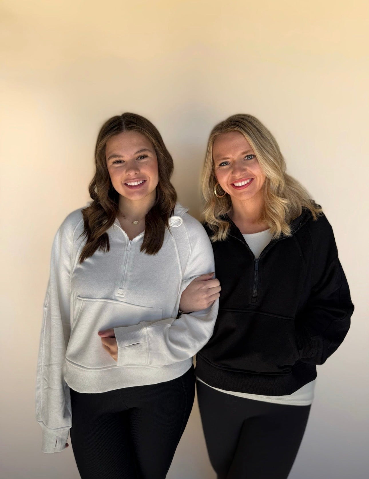 Two women standing side by side wearing matching outfits with a plain background