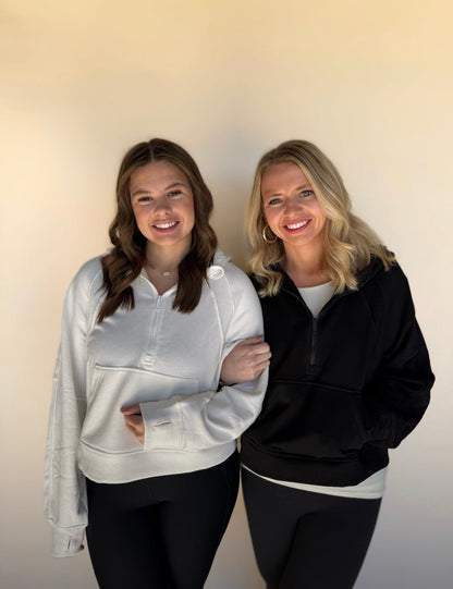 Two women standing side by side wearing matching outfits with a plain background