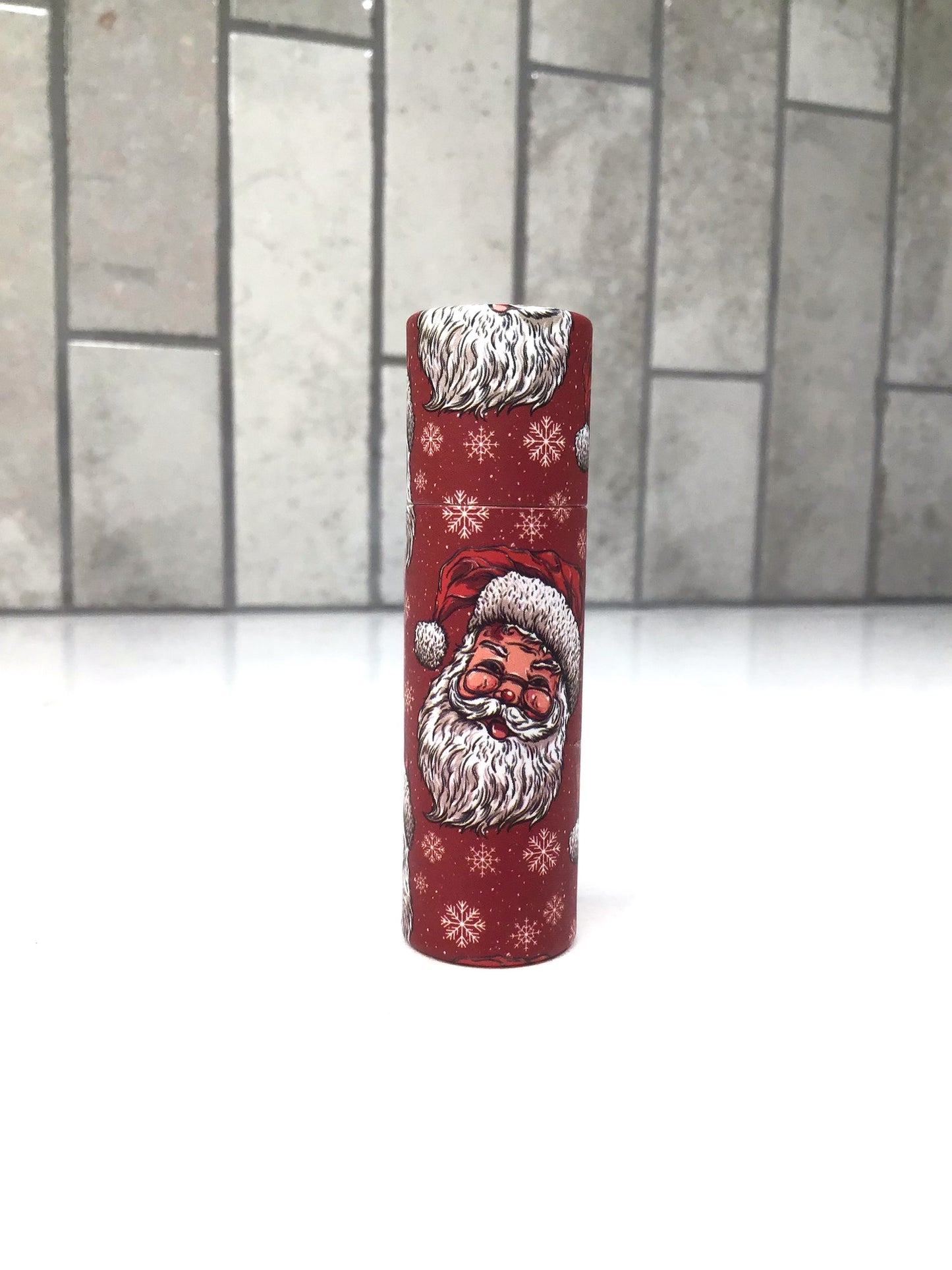 Red candle with Santa Claus design on a white surface with a gray tiled background