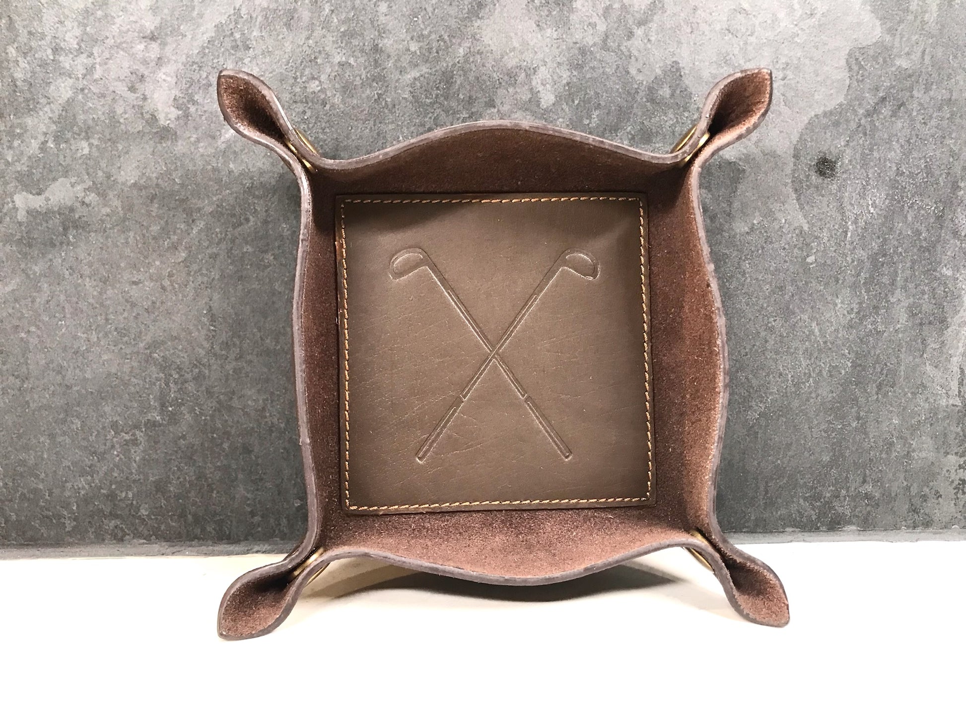 Brown leather catch-all tray with embossed design on a gray background