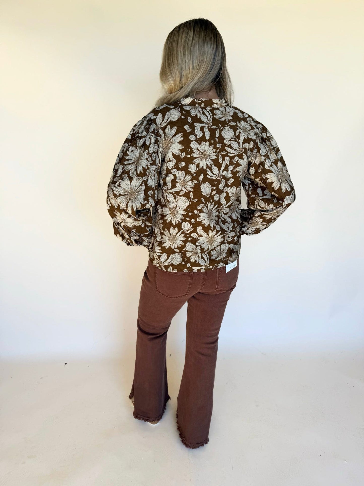 Back view of a brown floral long-sleeve blouse paired with brown flare pants.
