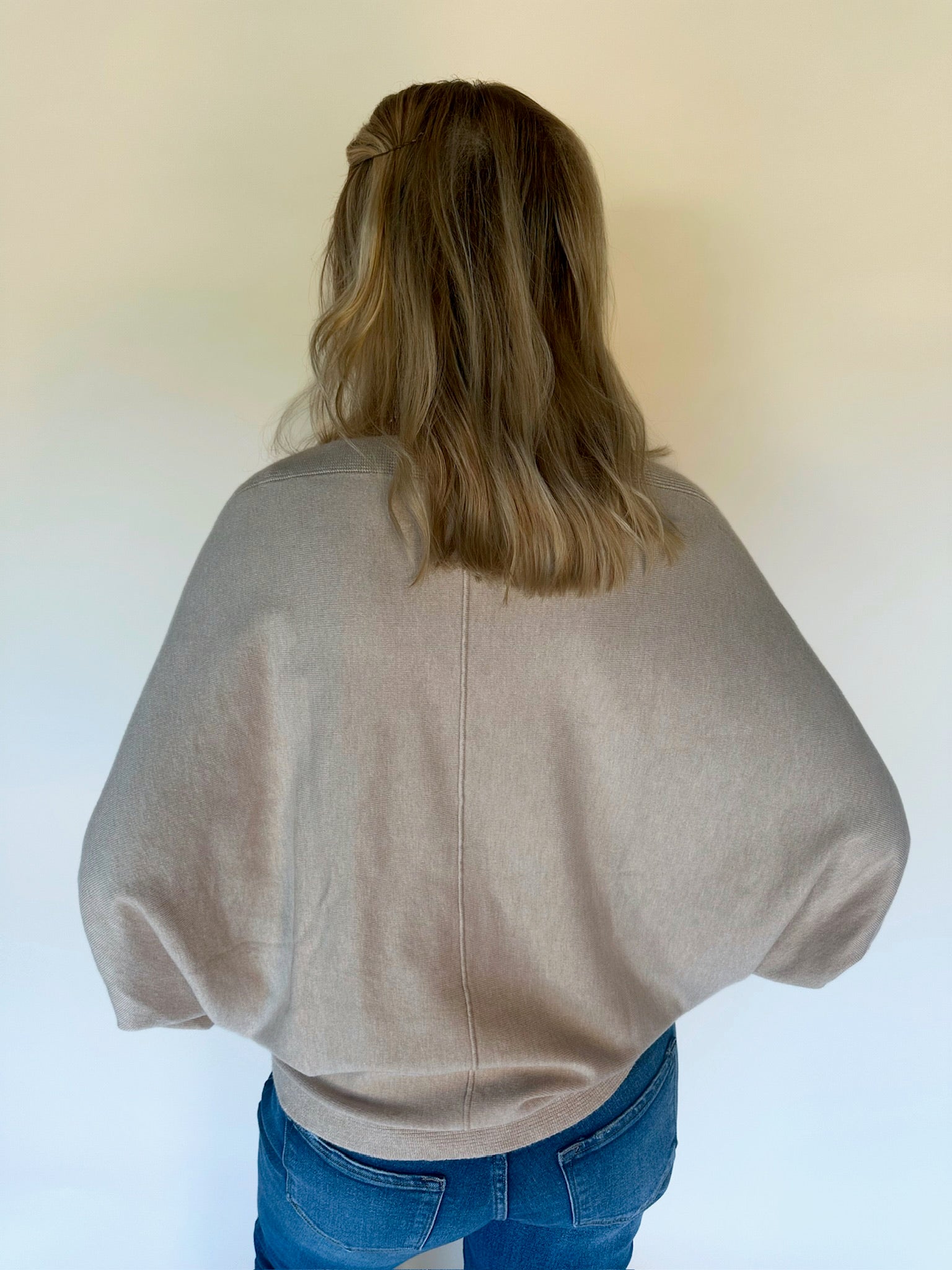 Person wearing an oatmeal sweater and blue jeans against a white background
