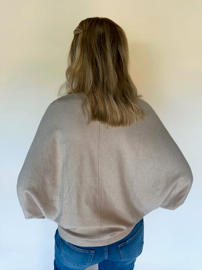 Person wearing an oatmeal sweater and blue jeans against a white background