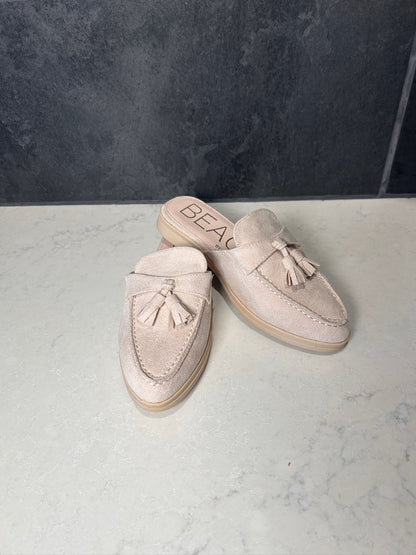 Pair of beige loafers with tassels on a marble surface with a dark textured wall background.
