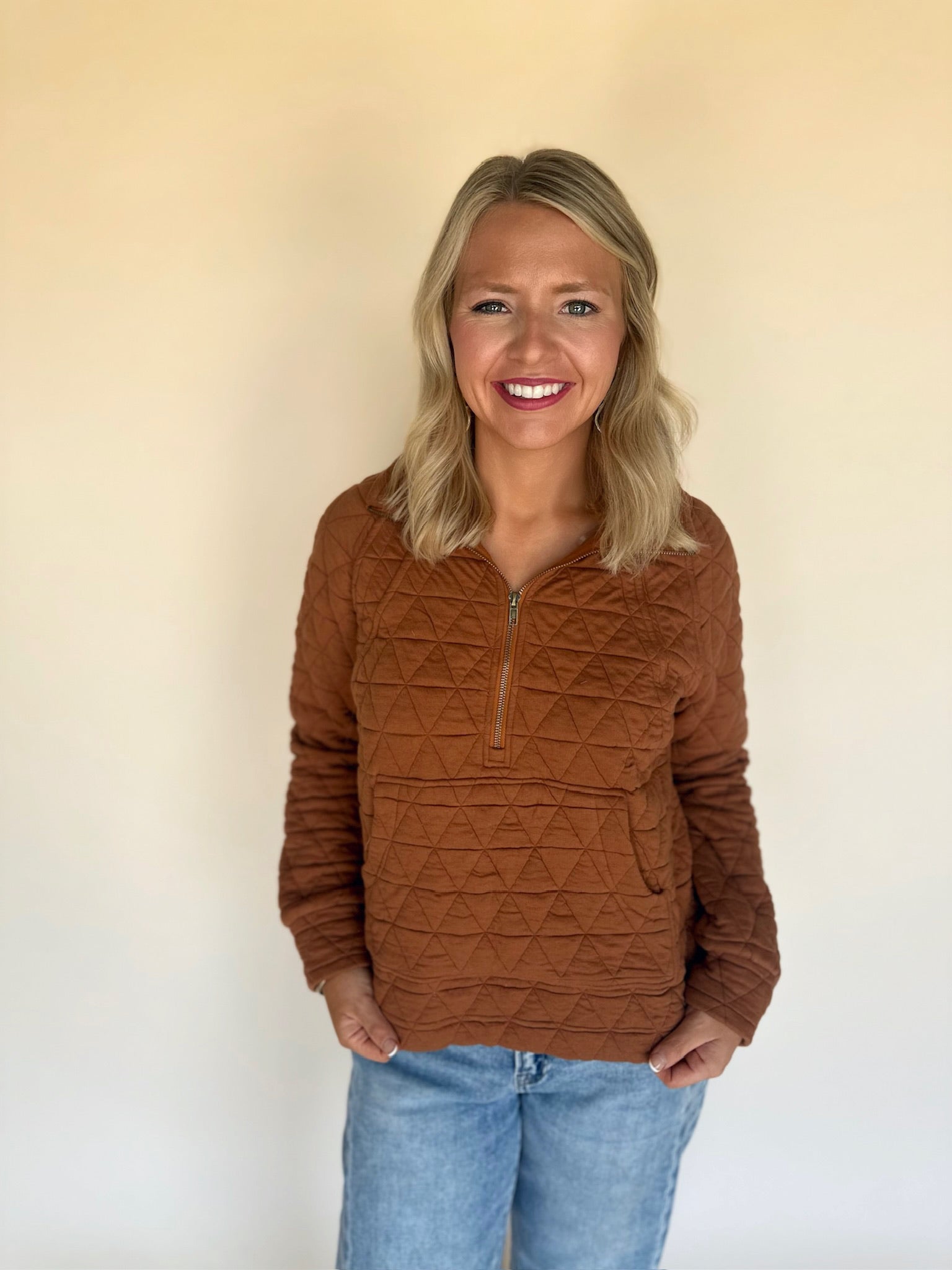 Woman wearing a copper quilted pullover with a plain background