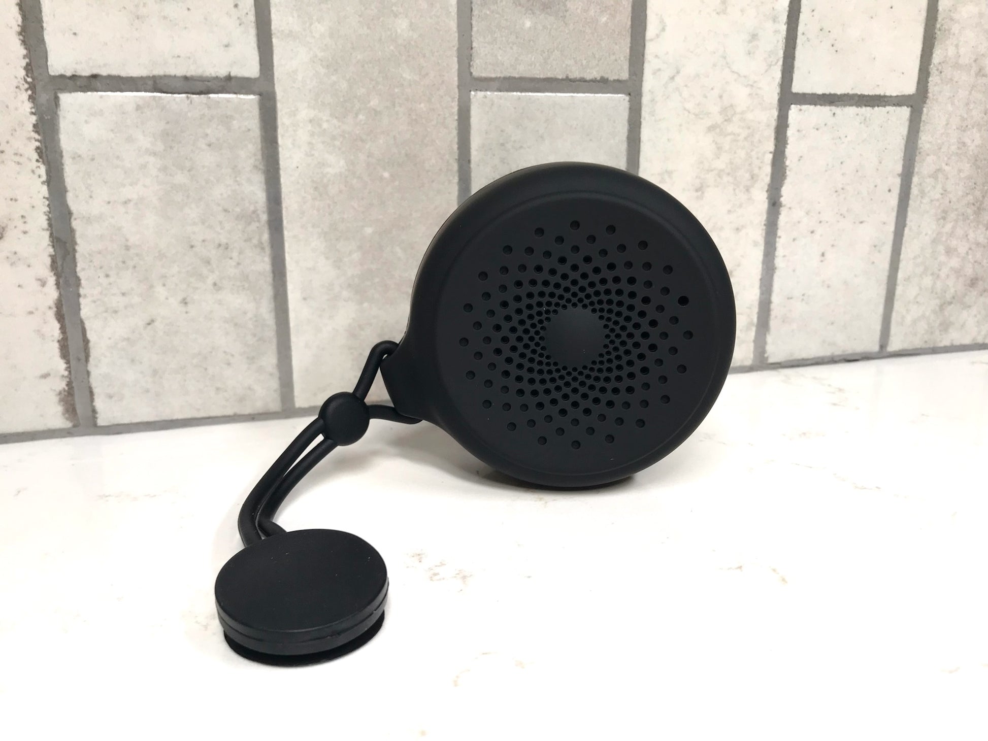 Black portable speaker on a white surface with a tiled wall background