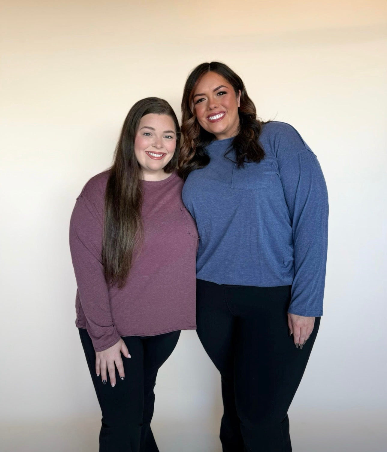 Two women standing side by side wearing long-sleeve shirts against a plain background