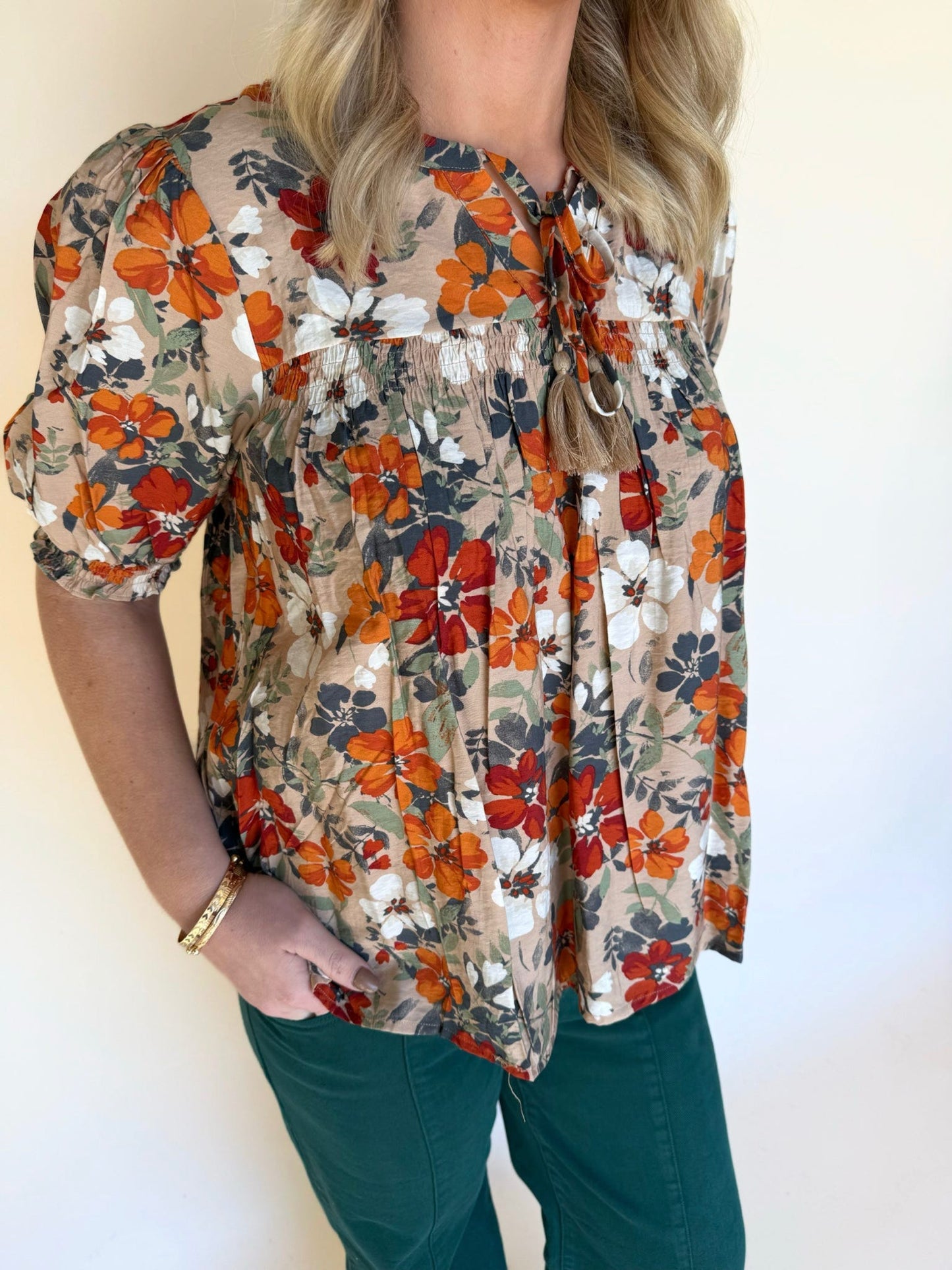 Side view of a floral puff-sleeve blouse with gathered bodice and fall-inspired colors, paired with green pants.
