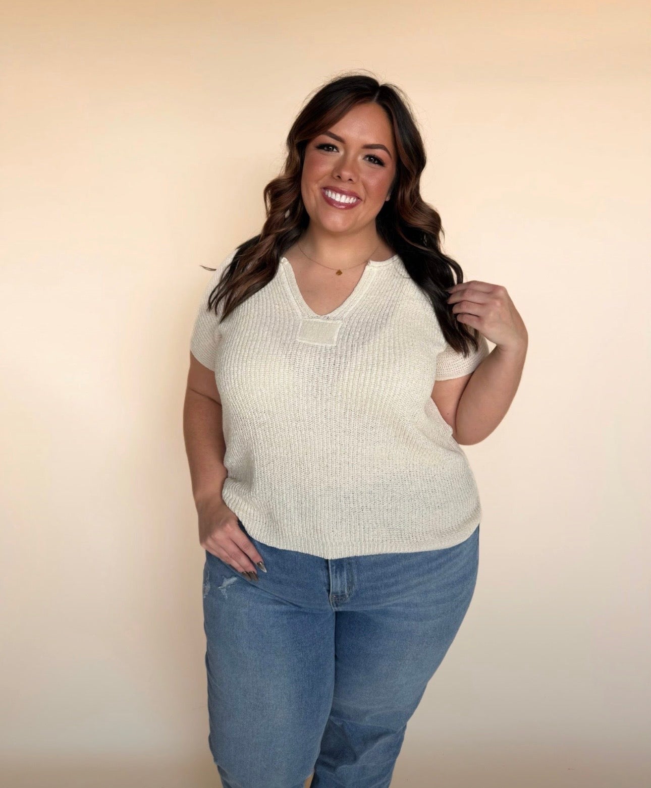 Woman wearing a cream short-sleeve sweater and blue jeans against a beige background