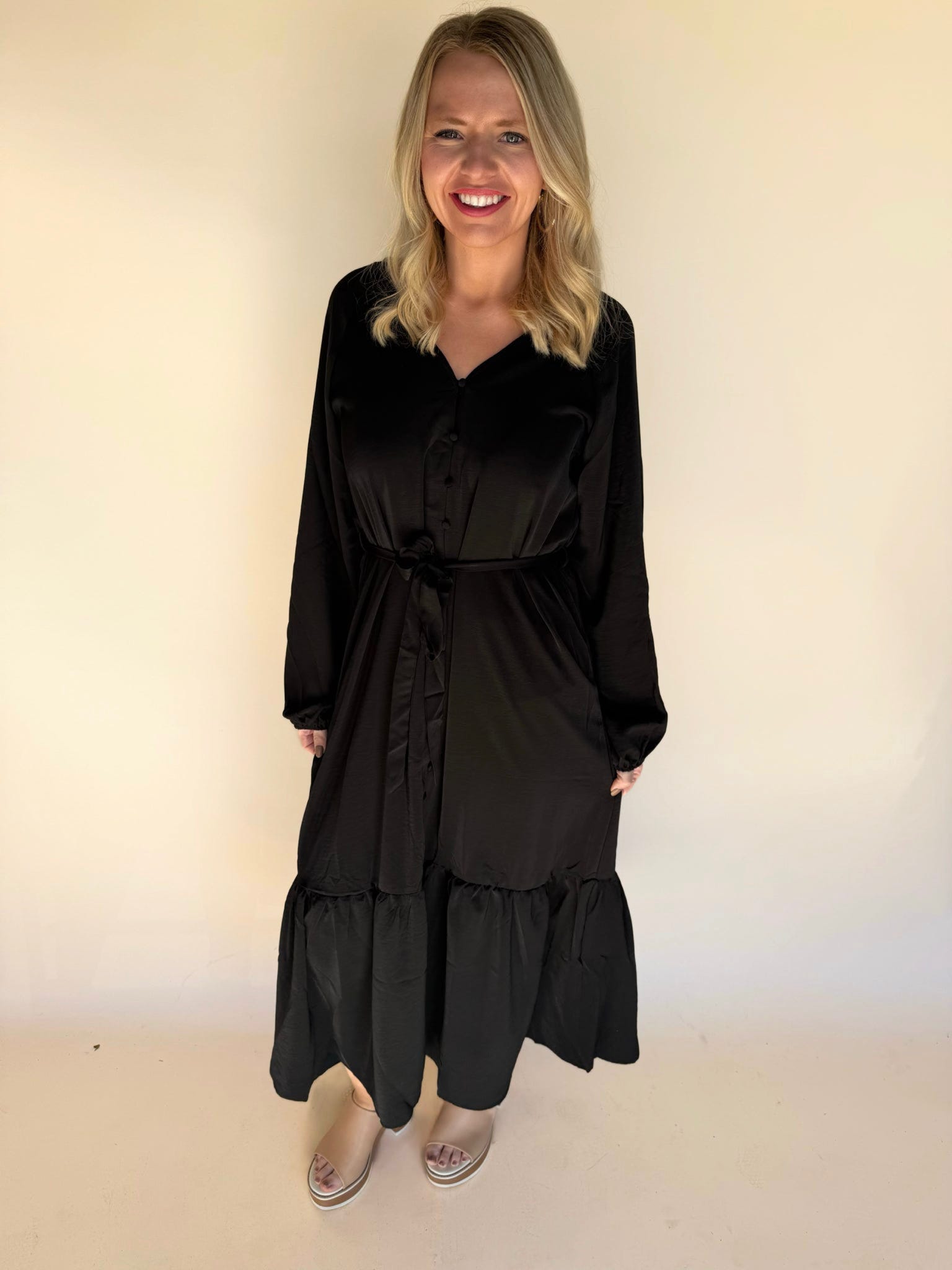 Woman wearing a black dress with long sleeves and layered skirt against a plain background