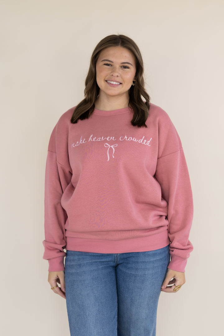 A woman wearing a dusty rose pink crewneck sweatshirt with white cursive embroidery that reads &