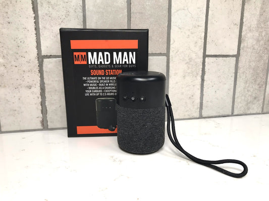 Black portable speaker with 'MAD MAN' branding and packaging on a textured surface.