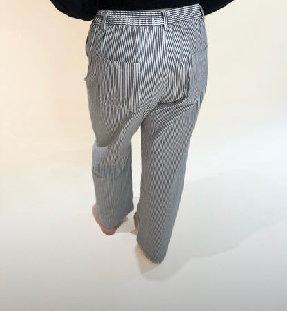 Back view of high-waisted black and white striped pants with patch pockets and straight legs, modeled barefoot against a neutral backdrop.