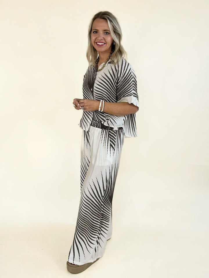 Ivory wide leg pants with a bold brown abstract print, elastic waistband, side pockets, and lightweight flowing fabric for effortless everyday wear.