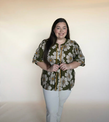 Woman wearing a floral blouse and white pants against a plain background