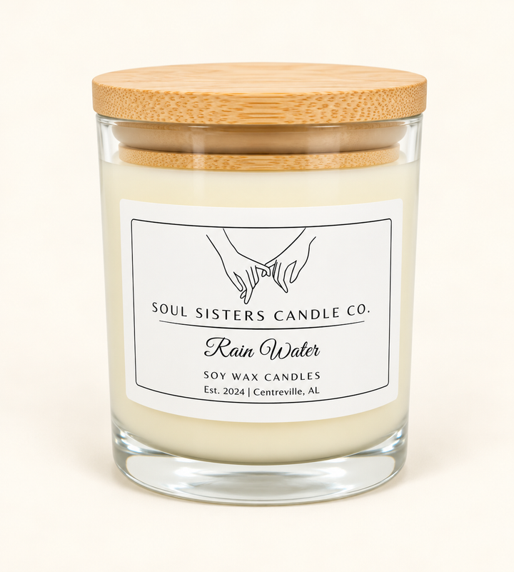Soul Sisters Candle Co. Rain Water scented soy wax candle in a clear glass jar with natural bamboo lid and minimalist white label on a cream background.