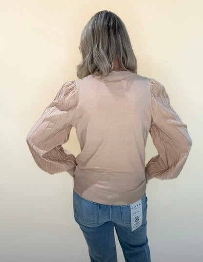 Back view of beige puff sleeve knit sweater showing ribbed sleeves and casual fit, paired with denim jeans.
