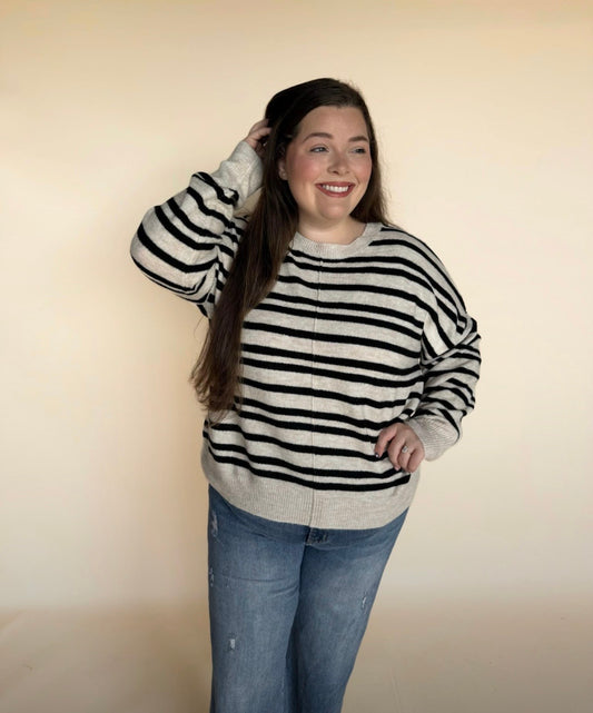 Person wearing a black and white striped sweater and blue jeans against a plain background