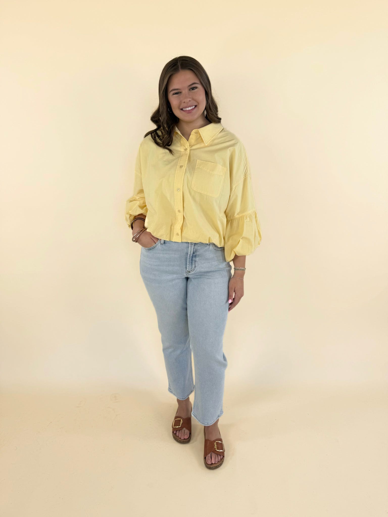 Woman wearing banana cream yellow bubble sleeve button-down top with light wash jeans and brown sandals