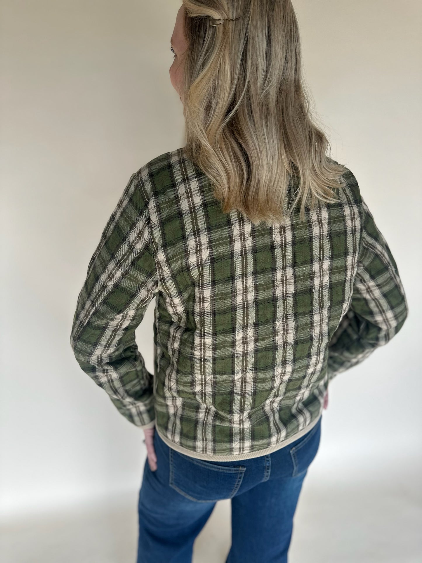 Back view of green and tan plaid jacket with long sleeves and soft flannel texture, shown on model wearing mid-rise blue jeans.