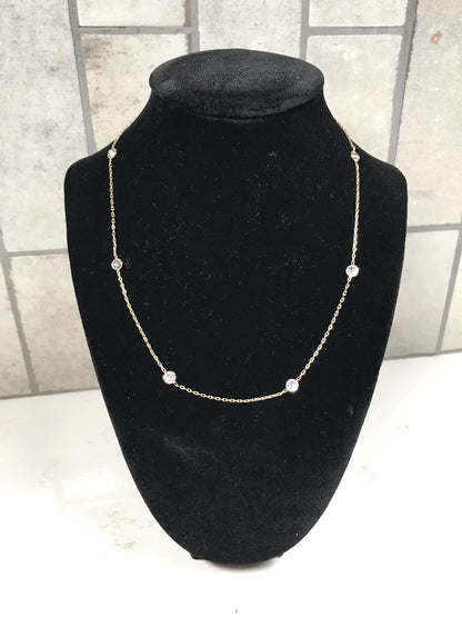 Gold dainty station necklace with small bezel-set clear crystals displayed on a black velvet necklace stand against a light tile background.