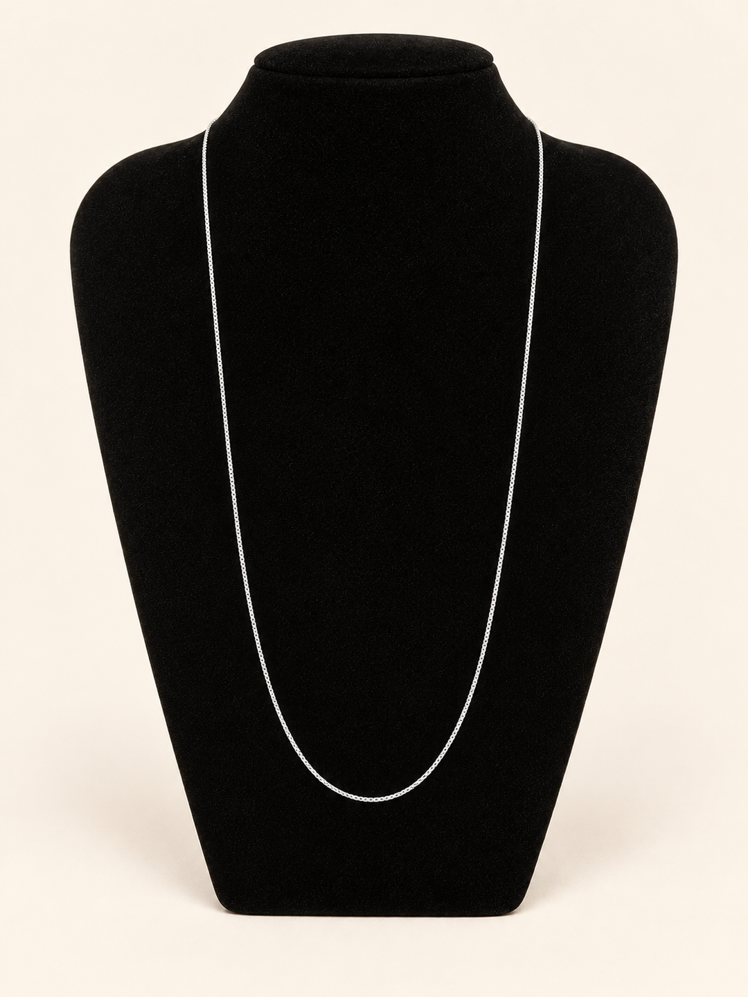 Delicate long silver chain necklace displayed on a black velvet jewelry bust against a cream studio background.