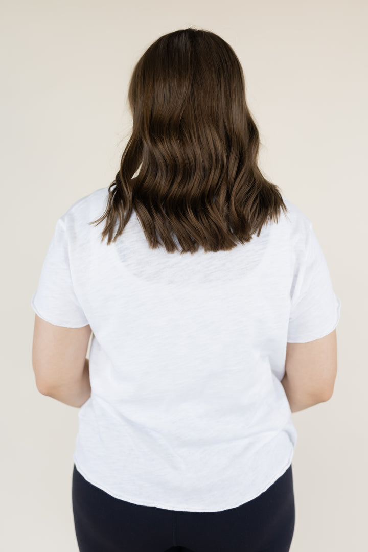 A woman viewed from behind wearing a white short-sleeve t-shirt and dark navy leggings, standing against a solid light beige background.