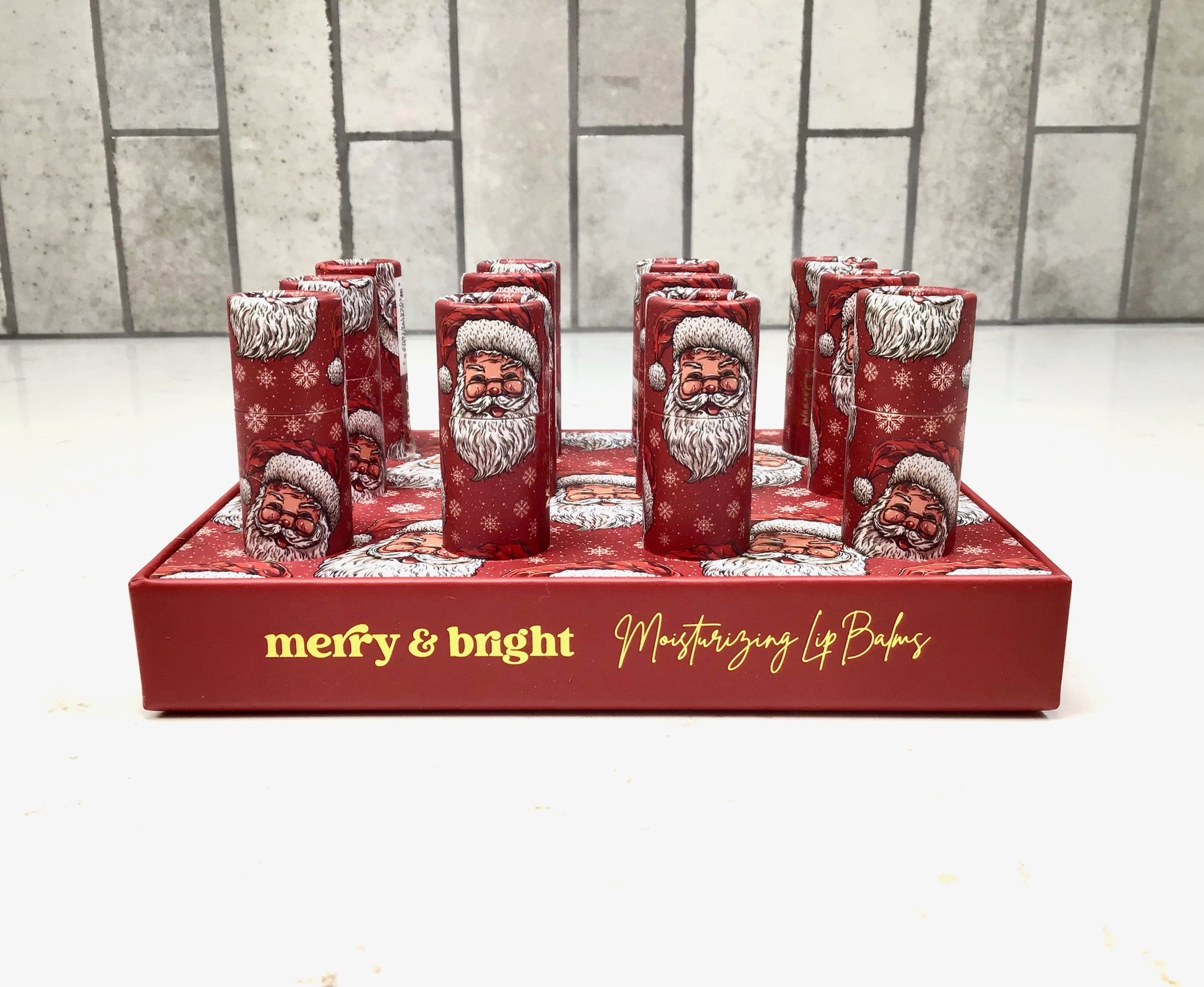 Set of red lip balm containers with Santa Claus design on a red tray with 'merry & bright' text.