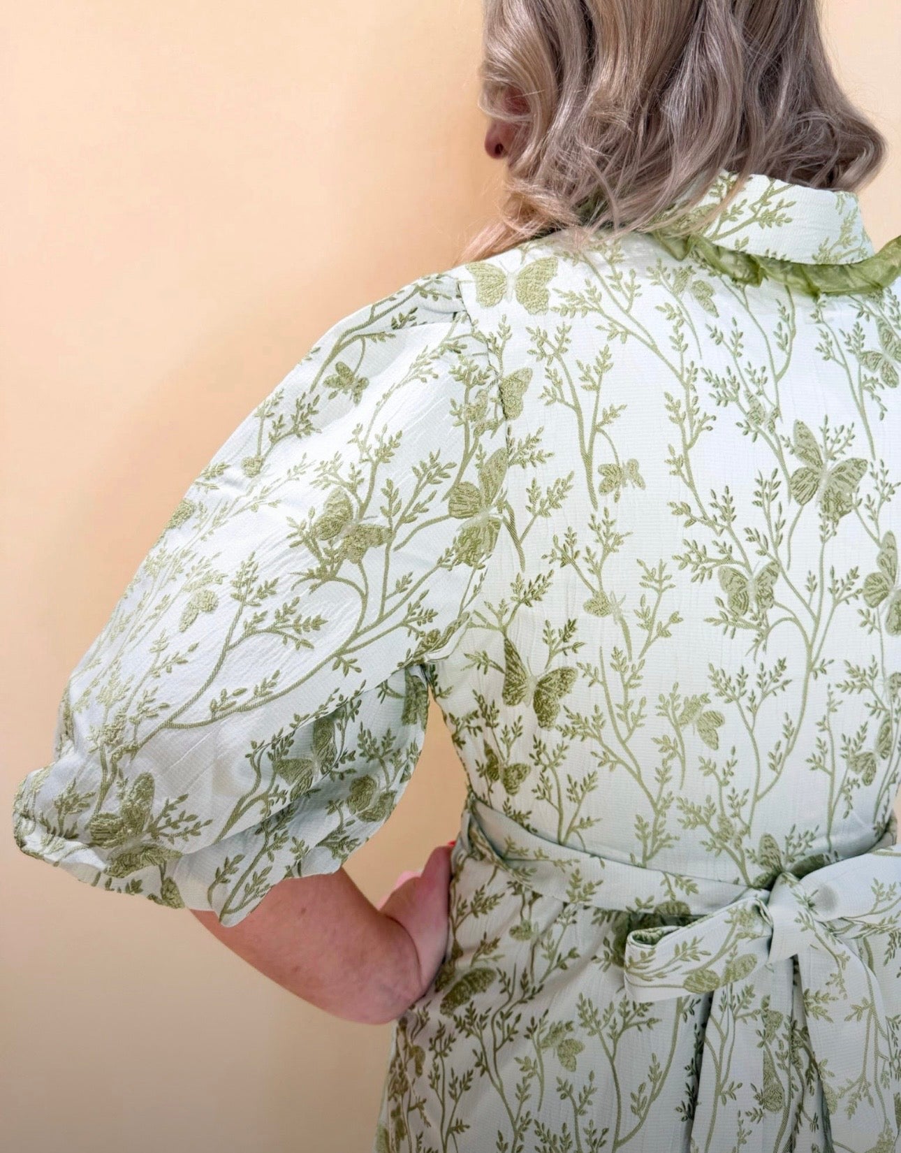 Detail shot of green floral midi dress displaying puff sleeves, tie waist bow, and woven botanical print fabric texture from the back angle.