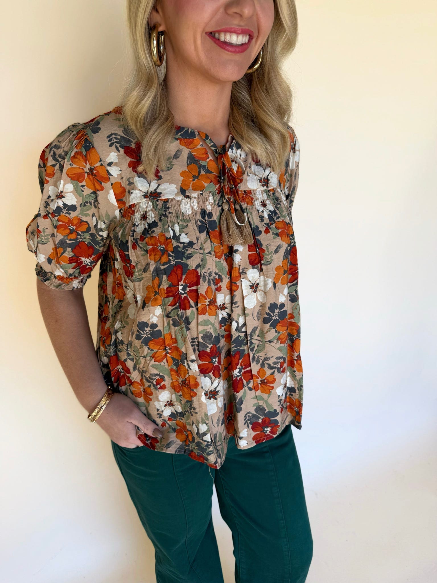 Close-up of a woman wearing a tan floral blouse with orange, white, and navy flowers, showing the tie neckline and gathered detail.