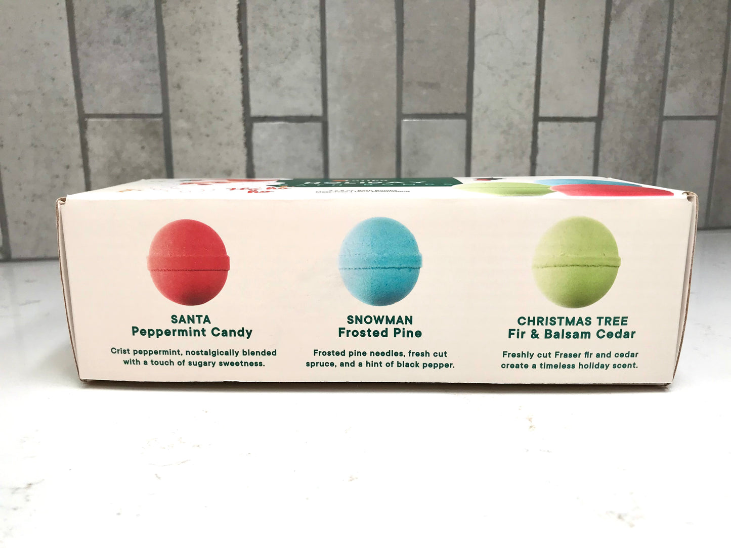 Box of scented candles with color-coded labels against a tiled wall background