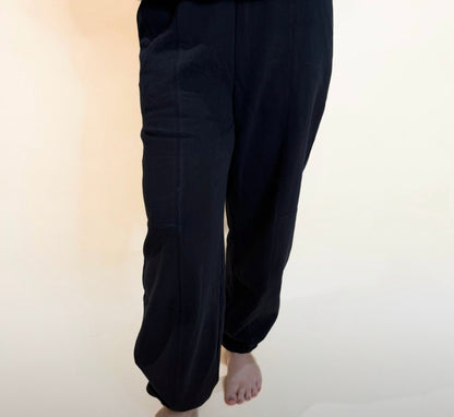 Black jogger sweatpants front view with relaxed fit legs and elastic cuffs, styled bare feet for casual look.