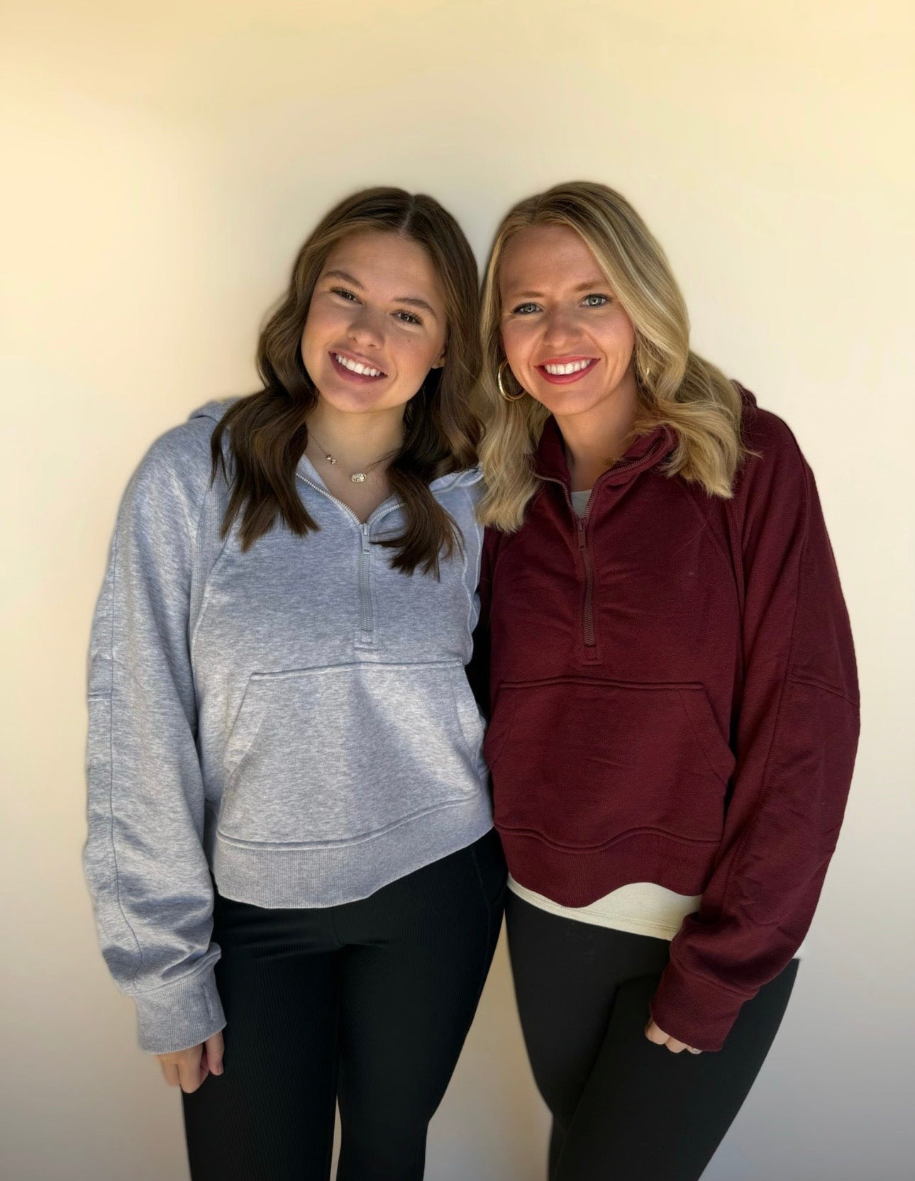 Two women wearing hoodies standing side by side against a plain background