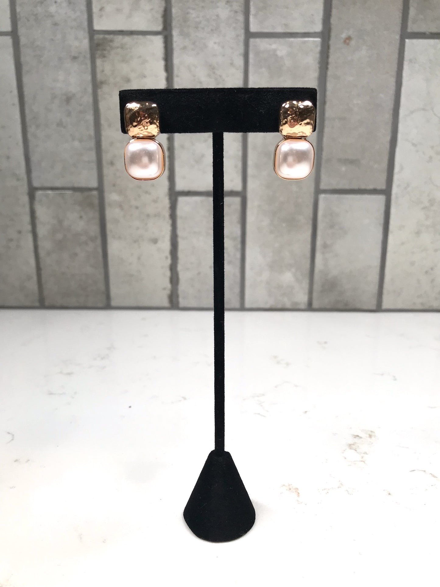 Gold hammered stud earrings with soft pearl drop stones displayed on a black earring stand.
