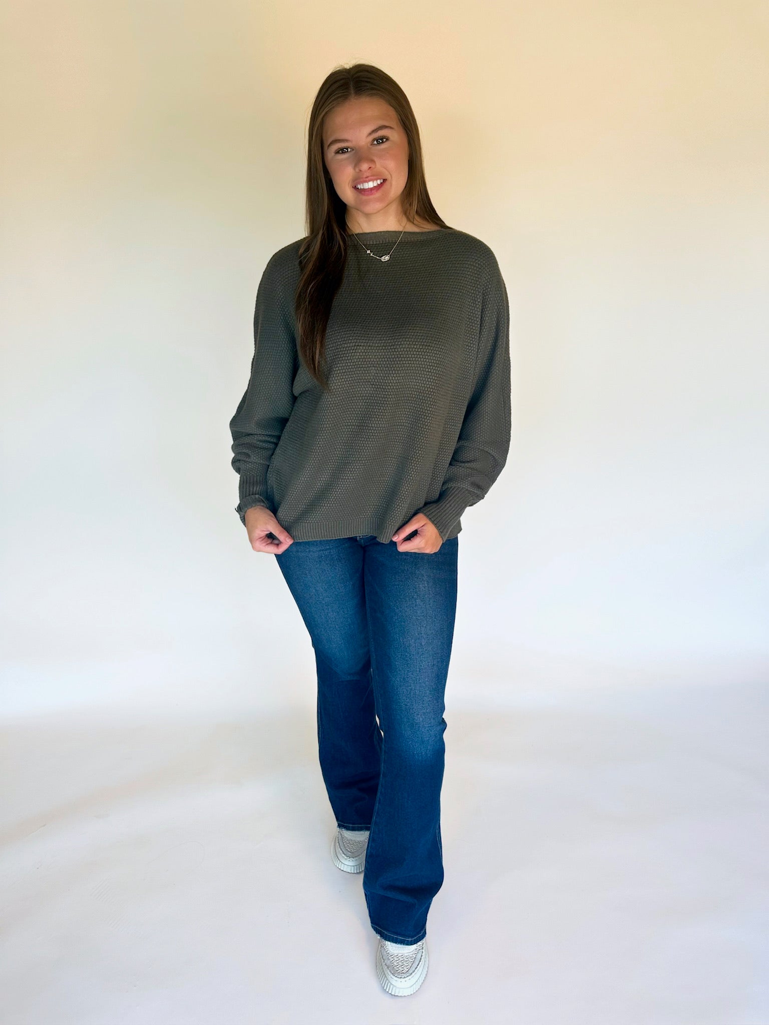 Woman wearing a green sweater and blue jeans against a white background