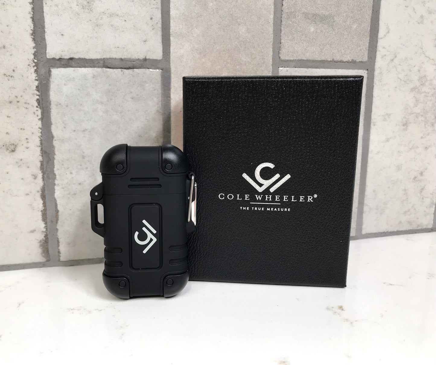 Black case with Cole Wheeler logo next to a black box with the same logo on a stone wall background