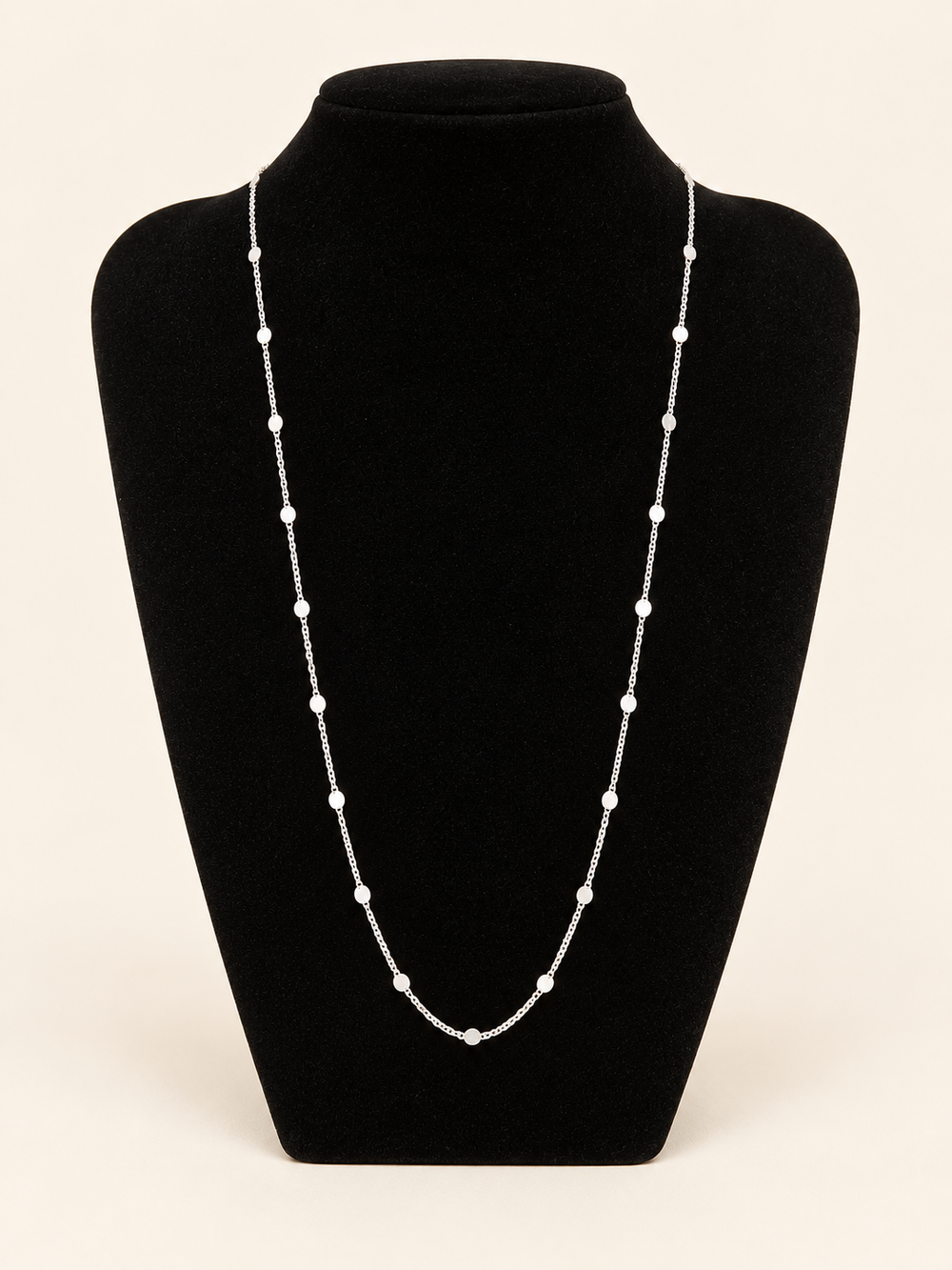 Long silver flat disc station chain necklace displayed on a black velvet jewelry bust with evenly spaced round accents.