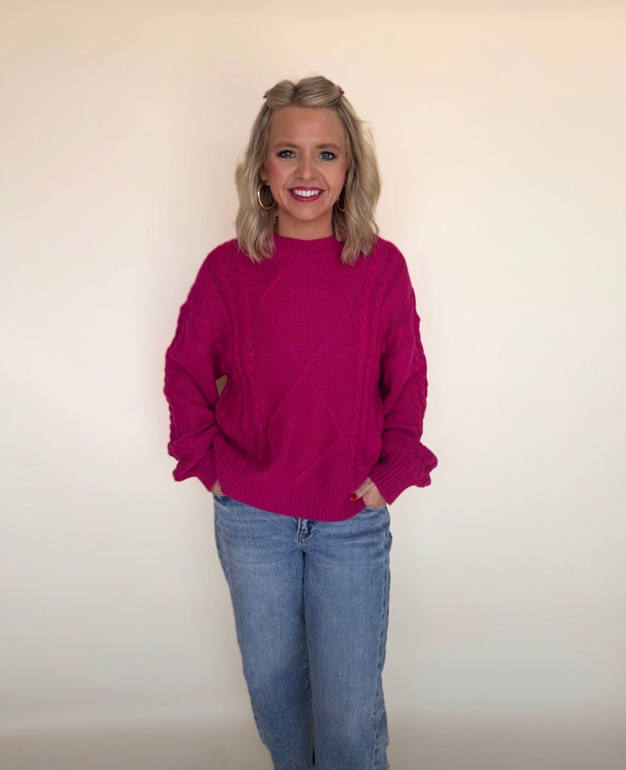 Woman wearing a magenta sweater and blue jeans against a plain background
