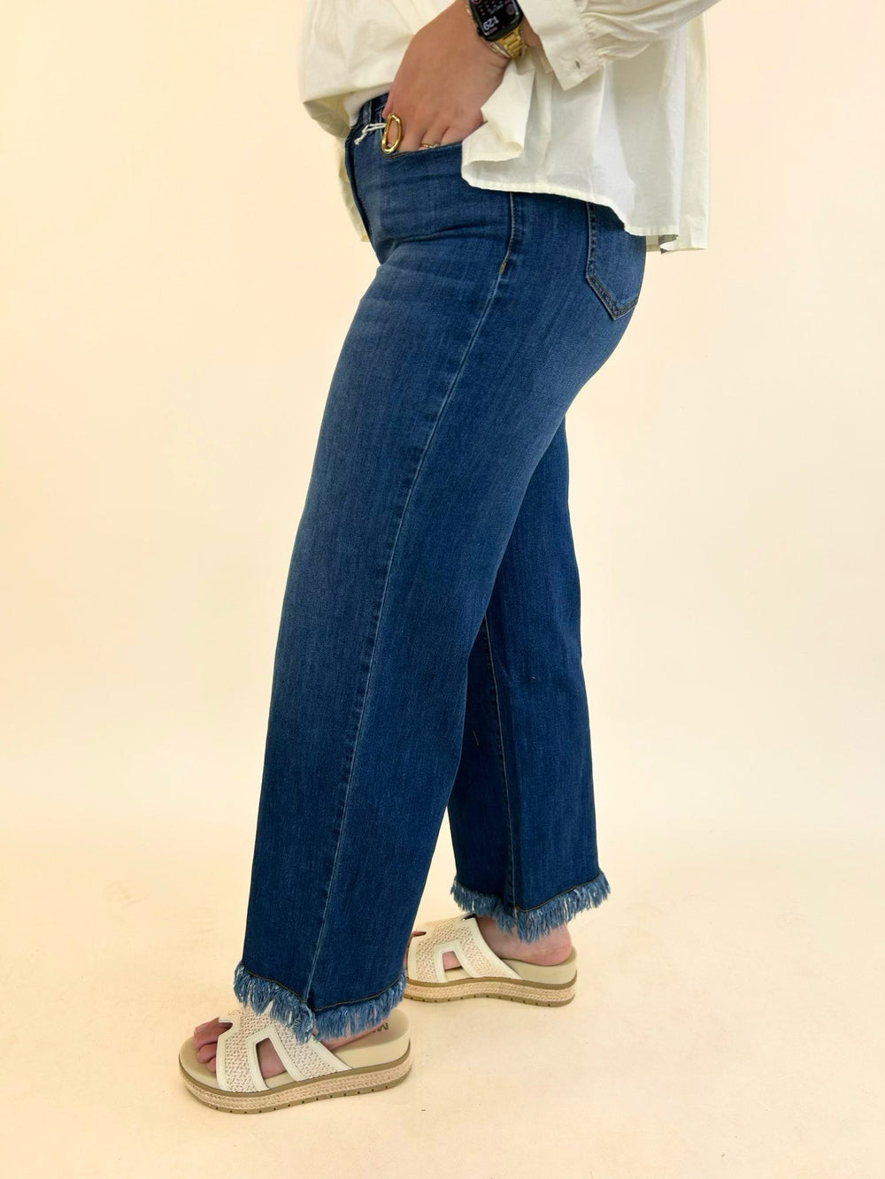 Side view of women's medium wash wide leg jeans featuring a high-rise waist and raw frayed hem.
