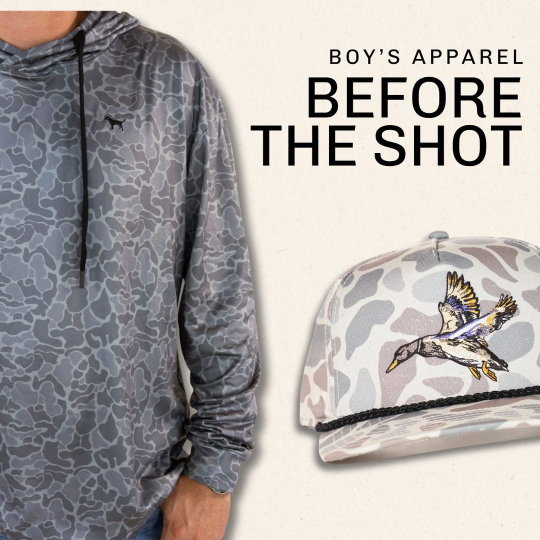 A promotional graphic for boy's apparel showing a cropped model wearing a gray and blue camouflage patterned long-sleeve hoodie on the left, and a matching camouflage baseball cap with a duck graphic on the right. Large text reads 'BOY'S APPAREL BEFORE THE SHOT' on a light beige background | Square 1 Boutique | Brent, AL