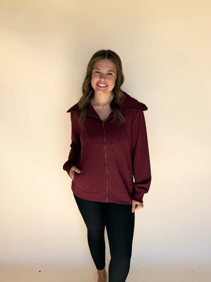 Person wearing a maroon jacket against a plain background