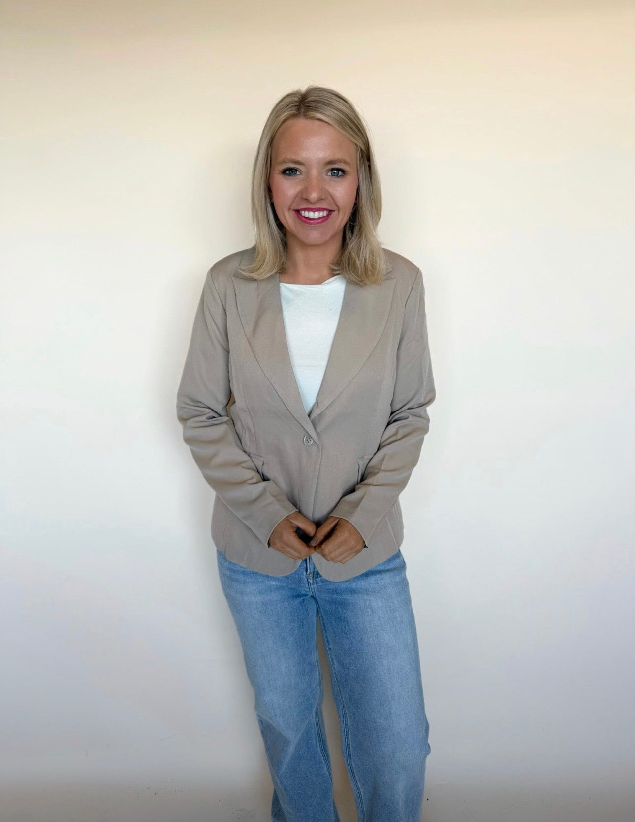 Woman wearing a beige blazer and blue jeans against a plain background