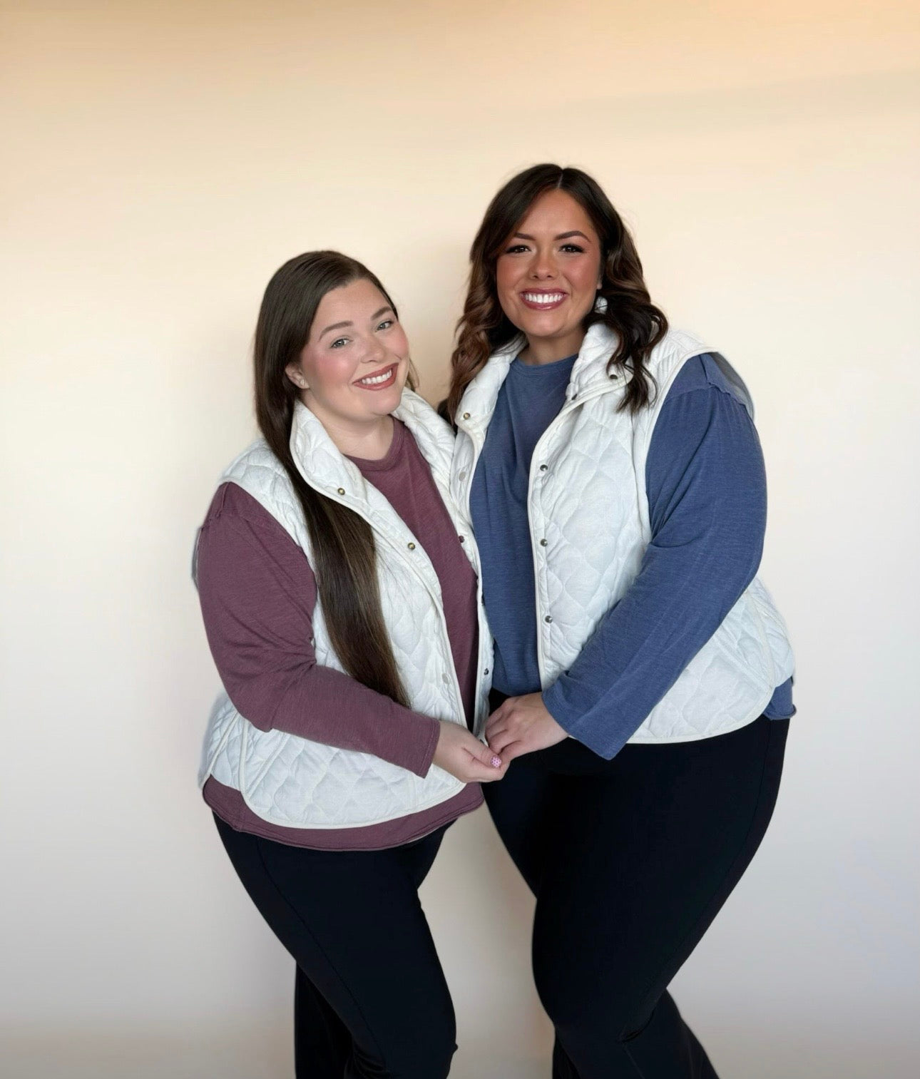 Two women wearing white quilted vests against a plain background