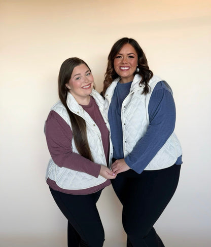 Two women wearing white quilted vests against a plain background