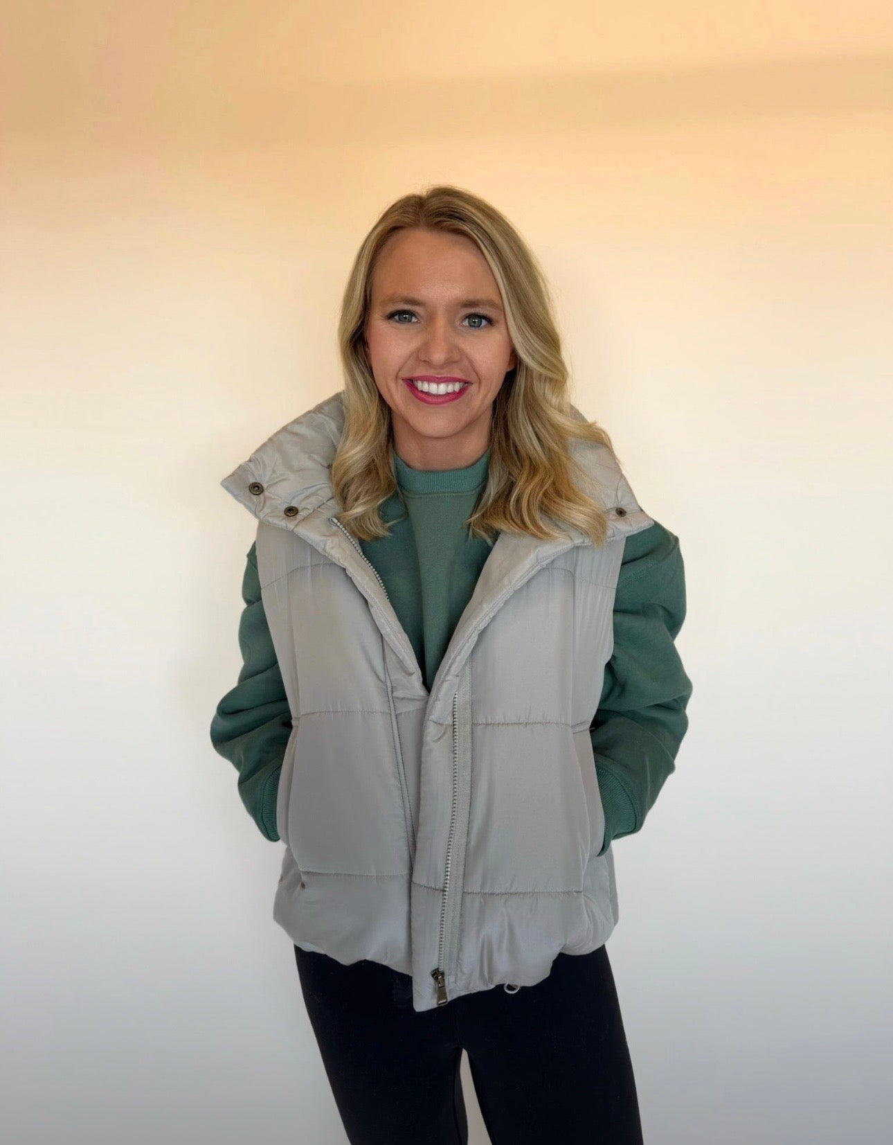 Woman wearing a green jacket with a gray vest over it against a plain background
