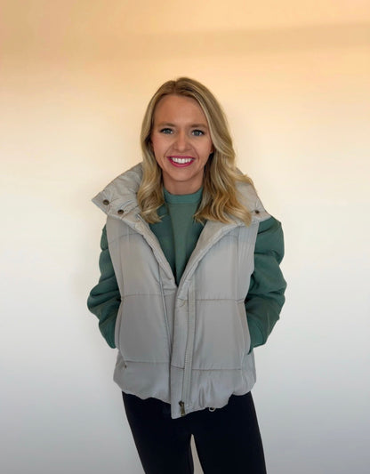 Woman wearing a green jacket with a gray vest over it against a plain background